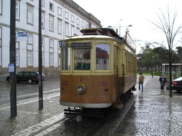 a trolley is traveling down a wet street with two cars and a person