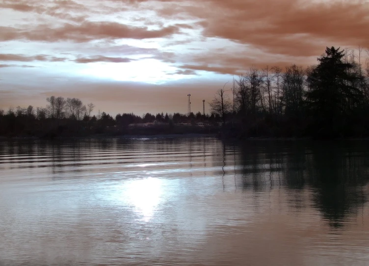 a lake surrounded by trees under a cloudy sky