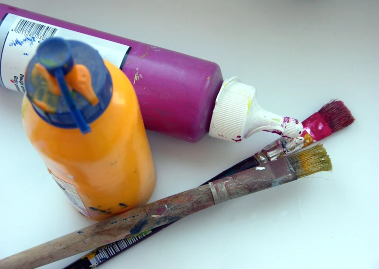 a white surface with three various colored paint and one empty bottle