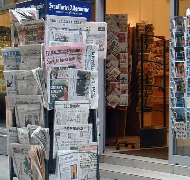 many newspaper stands in front of a building with various newspapers piled on top