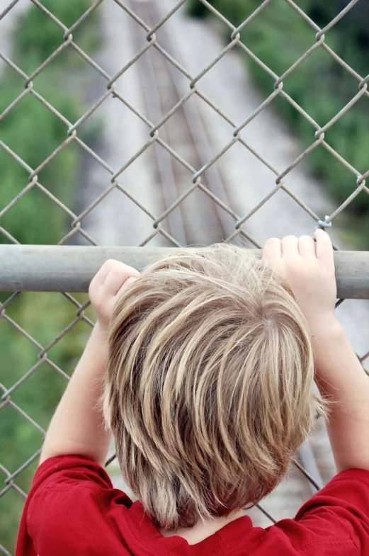 a boy leaning against a fence looking at railroad tracks