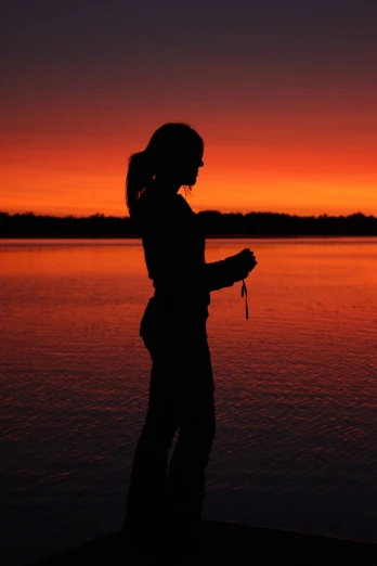 silhouette of woman with cellphone on waterfront at sunset