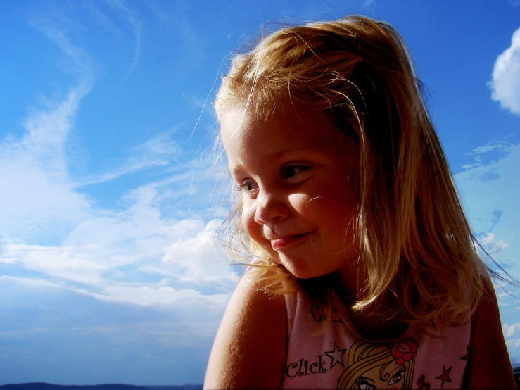 a little girl with long blonde hair standing in front of the ocean