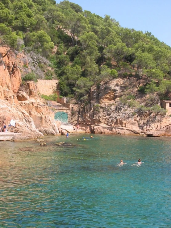 two people swimming in the sea near a rocky cliff