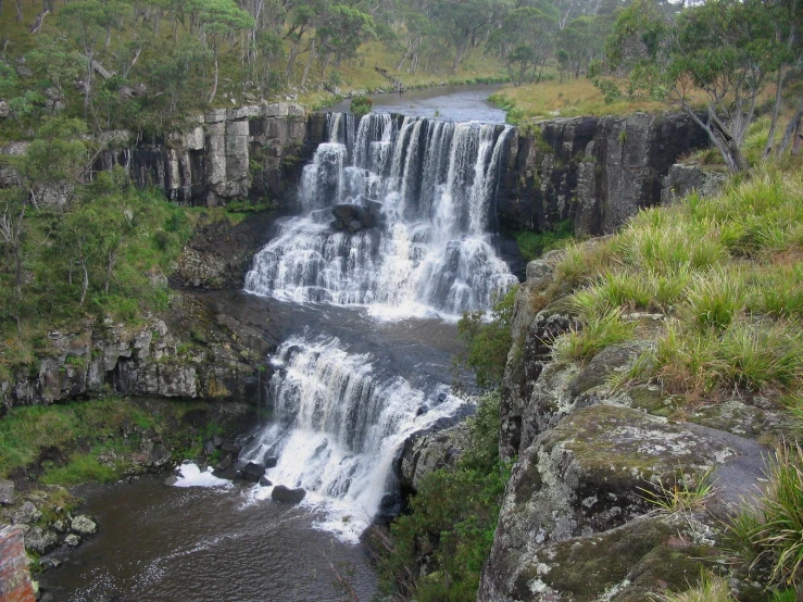 a waterfall with a river running through it near grass and trees