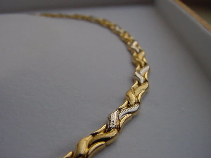 a gold and silver necklace on display with a black box