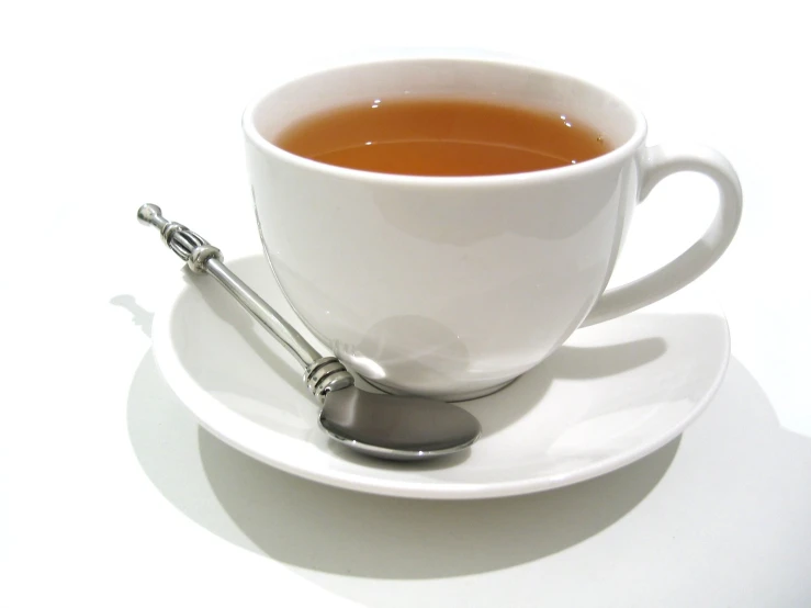 a cup with tea on a saucer next to spoon