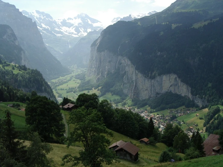 a valley with lush green hills, houses and snow covered mountains