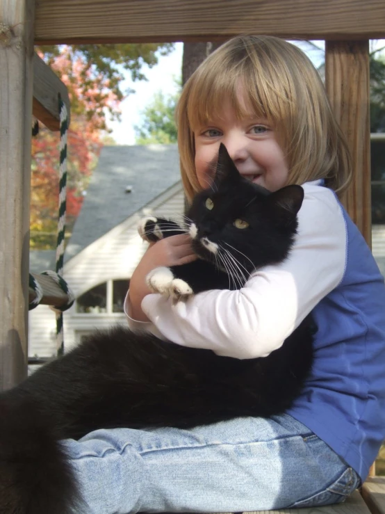 the girl smiles as she holds her black cat