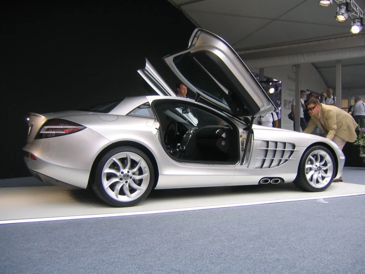 a man standing next to a silver car on display