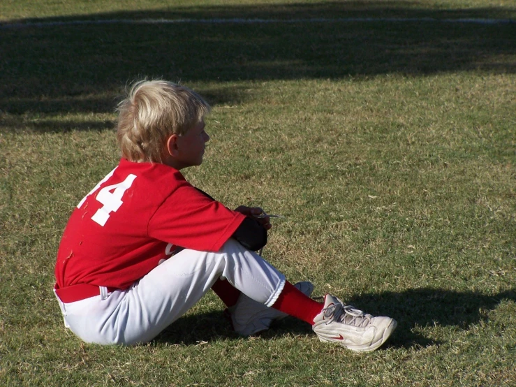 a child is sitting on the grass wearing a baseball uniform