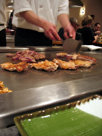 food being prepared on a grill with chefs in the background