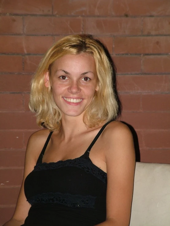 a girl in a tank top smiles in front of a brick wall