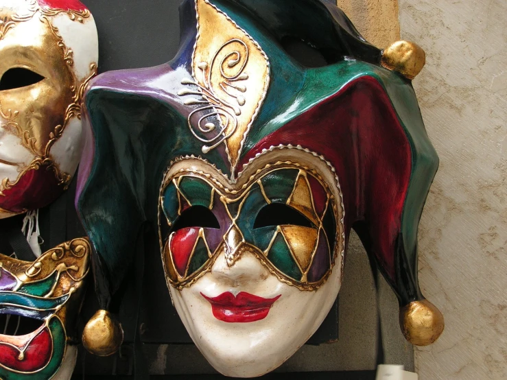 a green, red and gold colored mask with some bells around its neck