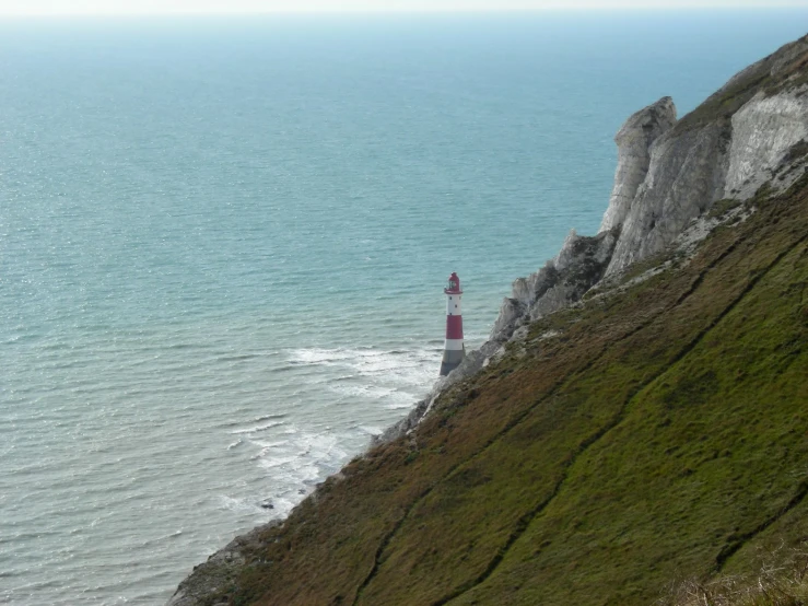 a small red light house on the side of a cliff by the ocean