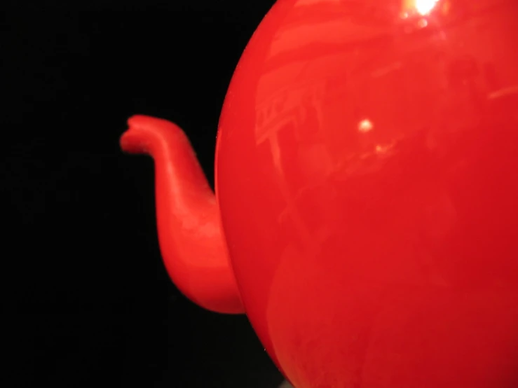 close up of a red teapot with a black background