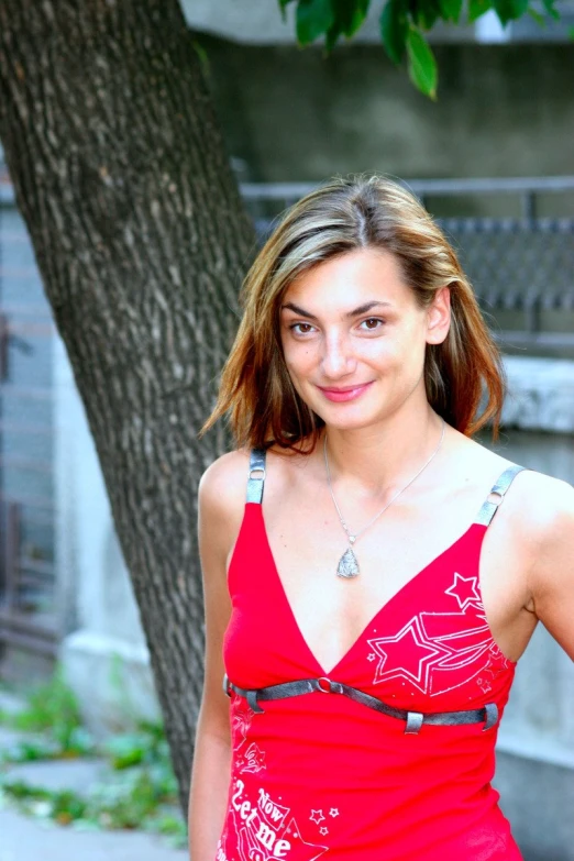 a girl wearing a red dress standing in front of a tree