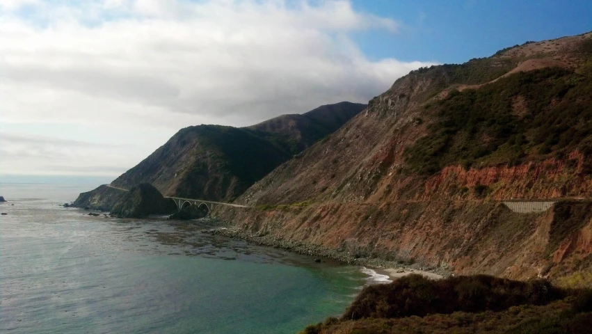 a hill side road and mountain with a body of water in front