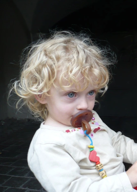 a small blonde toddler sitting with a chocolate treat in her mouth