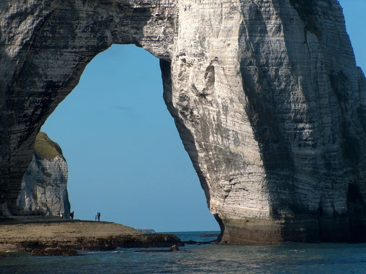 a large rock arch at the beach with some people in it