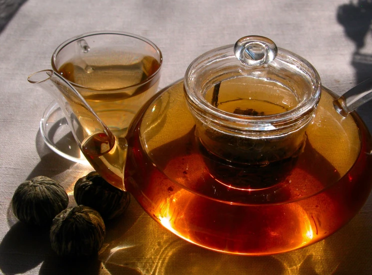 a glass tea pot with a cup of tea next to it