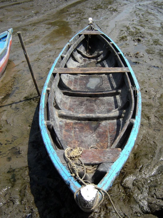 a small boat in the mud with one sitting next to it