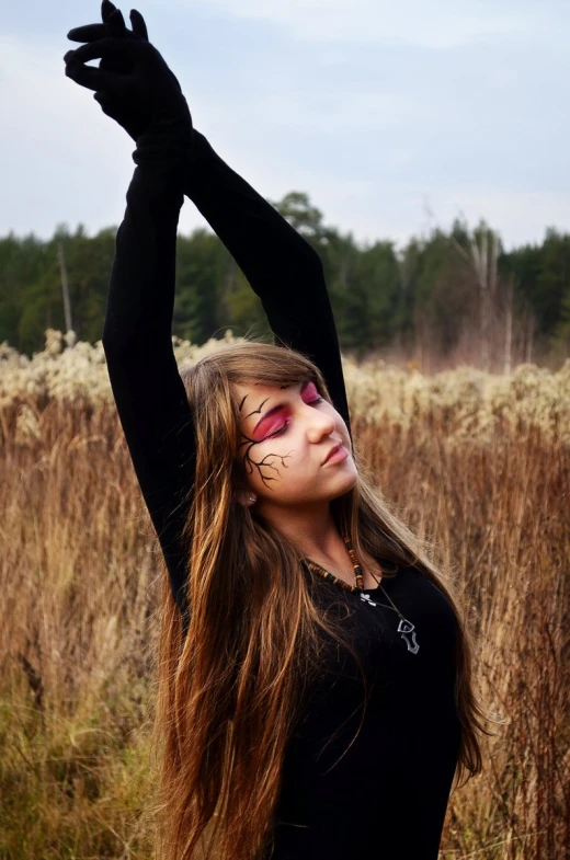 a woman is standing in some tall grass wearing face paint