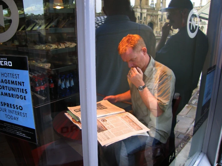 a man sitting in front of a shop window reading a newspaper