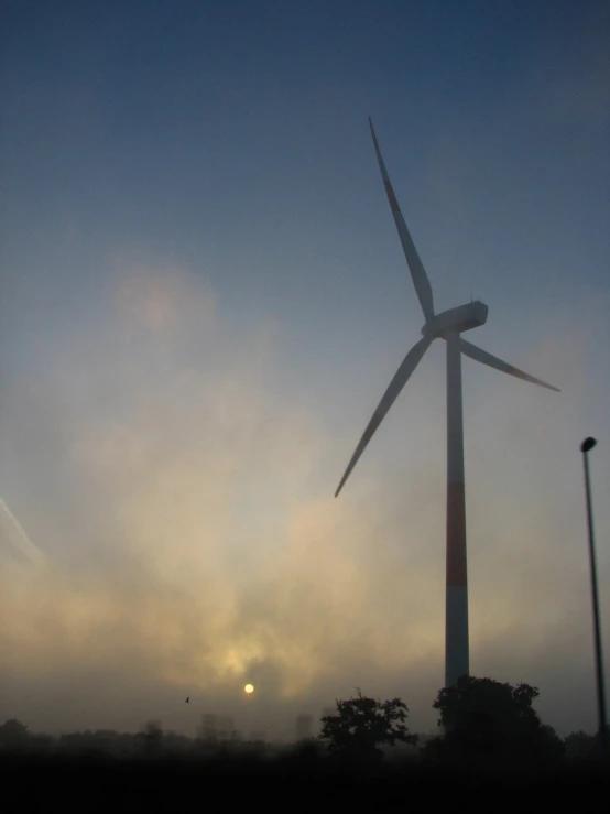 the top of a wind farm with trees, clouds and sun in background