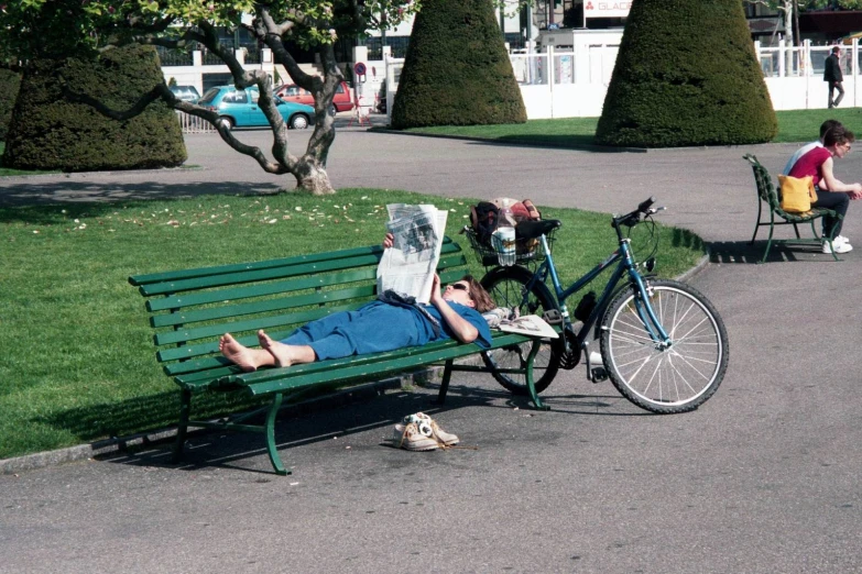 a woman lies on a park bench while a dog is beside her