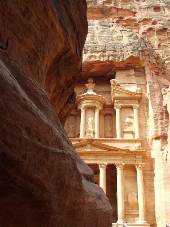 several people are standing near a building built inside of a large rock cliff