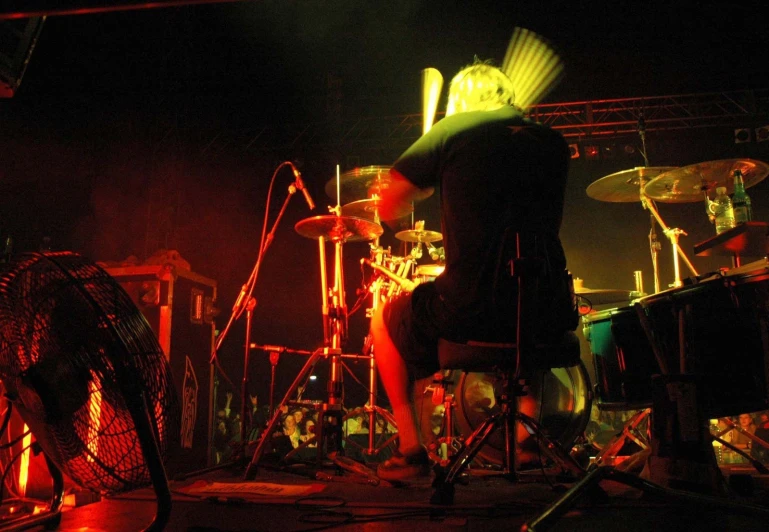 a man standing on stage next to a set of drums