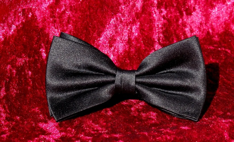 a black bow tie sitting on a red velvet blanket