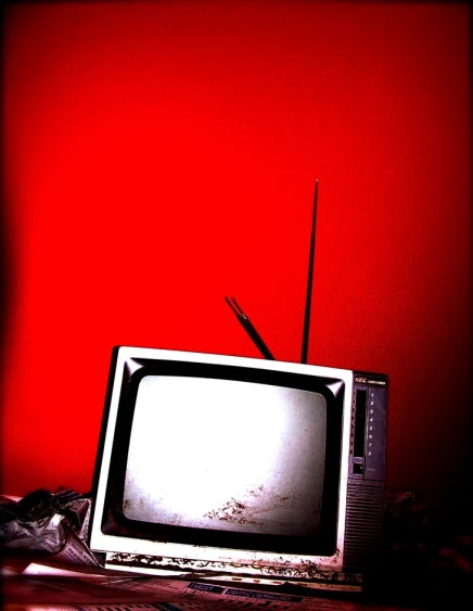 an old tv on a table near a red wall