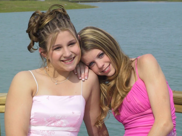 two young women sit next to each other near a lake