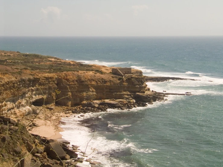 a rocky cliff overlooking the ocean with water below