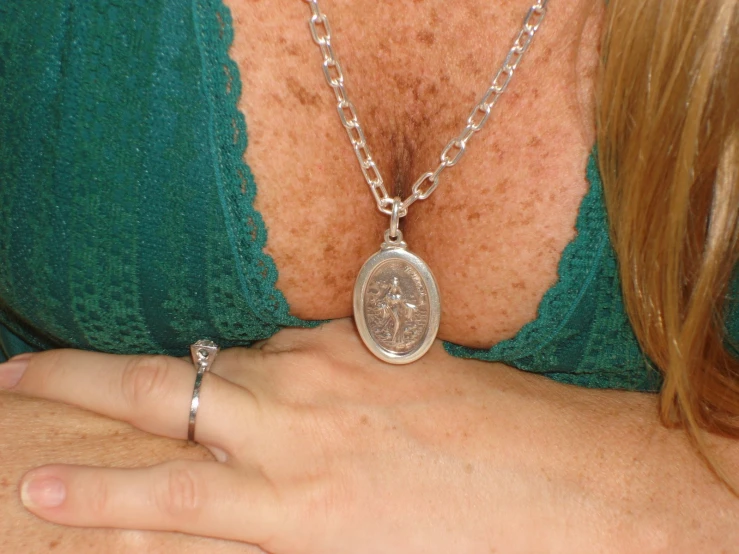 a person wearing a silver chain necklace with an engraved coin pendant attached to their chest