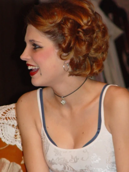 a woman sitting with her lips open and wearing a necklace with a diamond