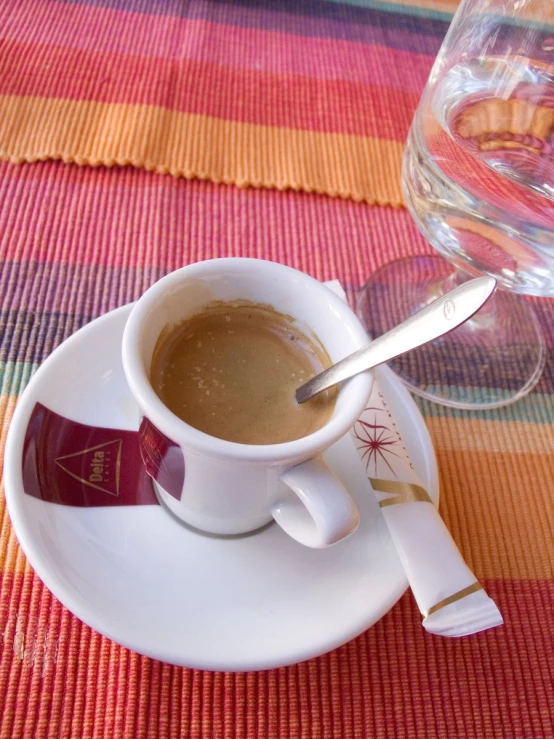 a cup of coffee next to a spoon on a white plate