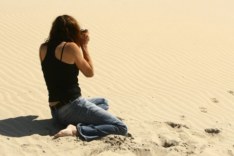 the woman sits on the sand and takes her picture