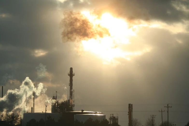 a factory with smoke stack and sky filled with clouds