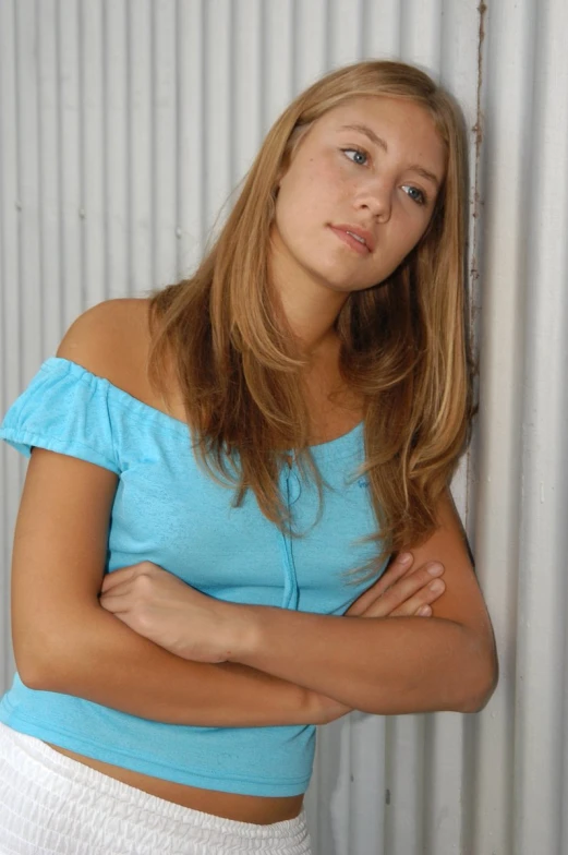 a young blonde haired woman with her arms crossed, leaning against the wall