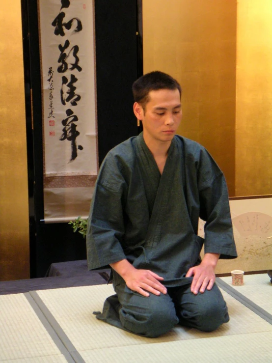 a man is seated on a mat near a buddha scroll