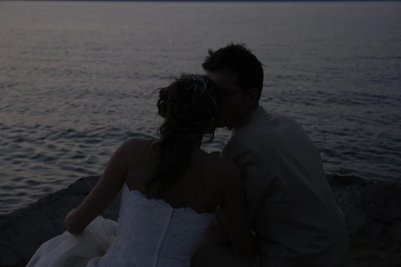 a young man and woman sitting together by the ocean