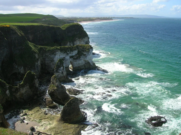 an ocean cliff face with blue water and green land