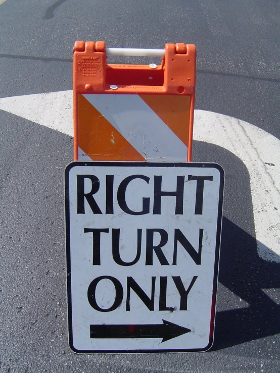 an orange and white street sign next to a road