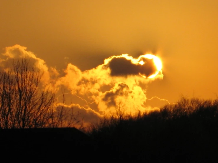 the sun behind some clouds over trees