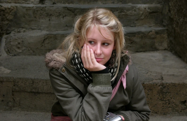 a young woman sits on the steps, covering her face with both hands