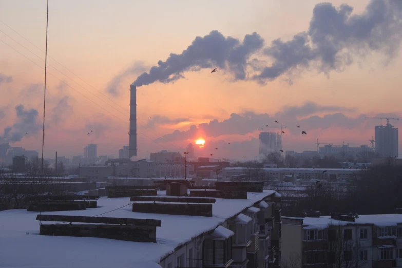 the sun is setting over an industrial area in the snow