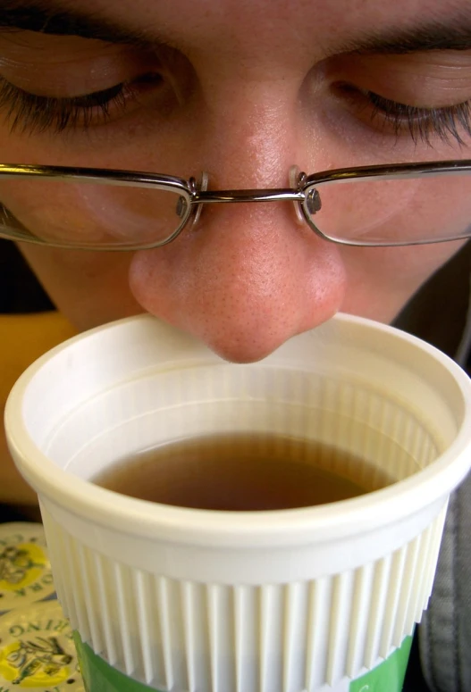 a close up of a person with glasses on while drinking coffee